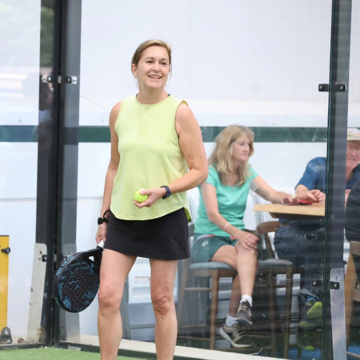 Smiling club player holding a blue and black FLO padel racket before serving