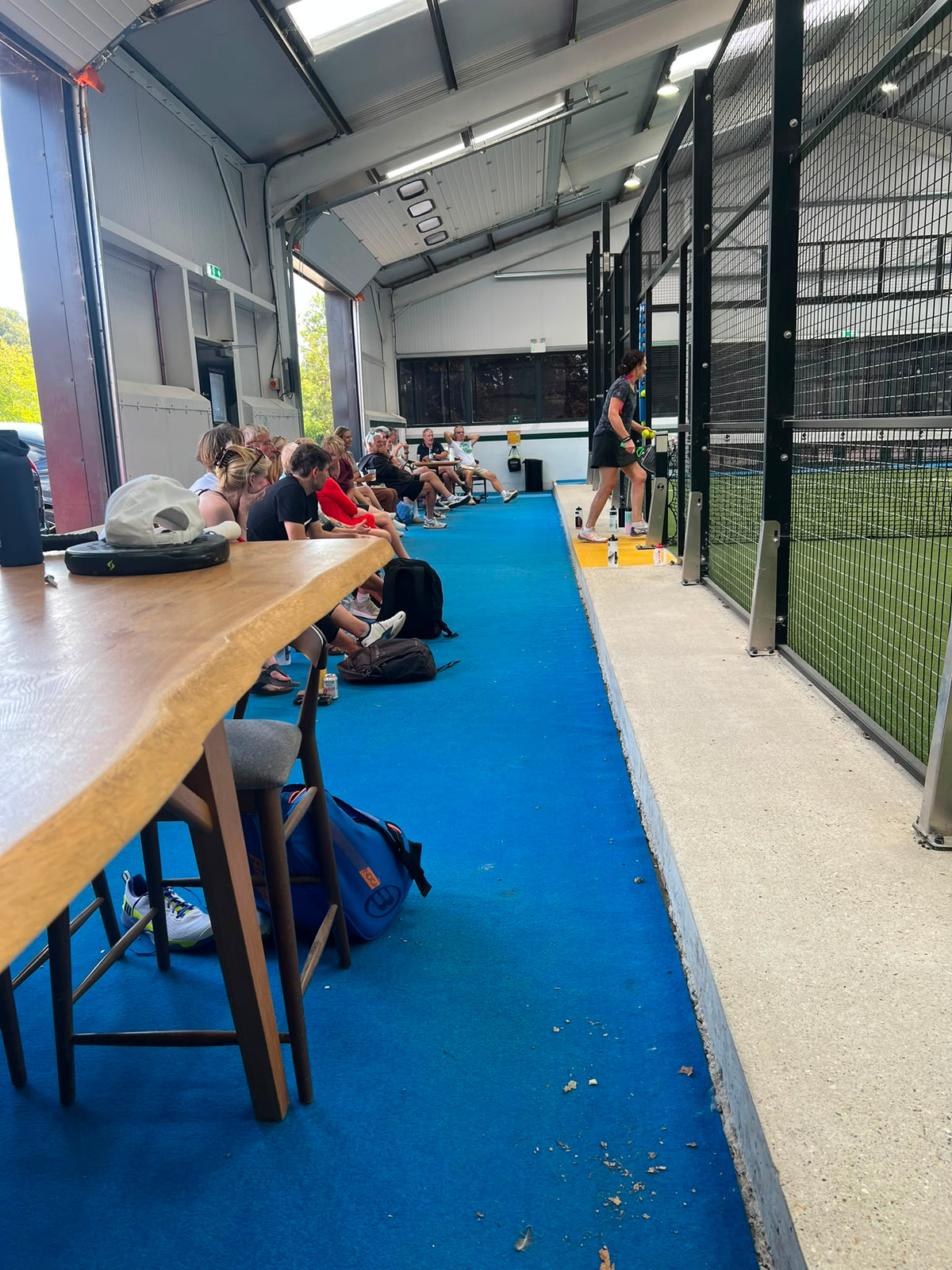 Club players and spectators gathered beside an indoor padel court at The Barns at Wellington